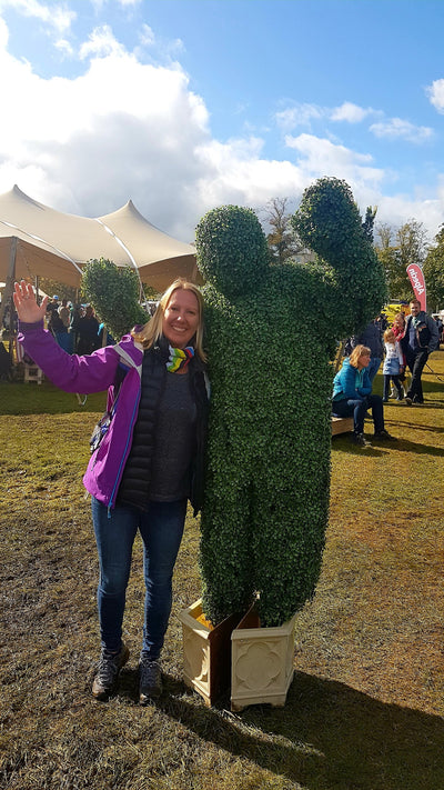 Woman wearing her world champion rainbow Ruffnek neck gaiter as a supporters scarf whilst watching the UCI cycle race and bumped into a giant hedge man!