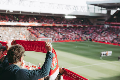 Person holding a red and white scarf in a football stadium with the football pitch in the background. Ruffnek snoods the offside rule.