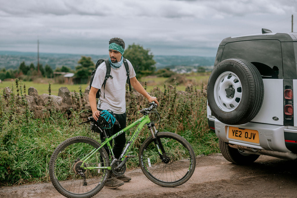Man with mountain bike wearing a Ruffnek headband and neck gaiter stood next to a Landrover Defender in the Yorkshire Countryside