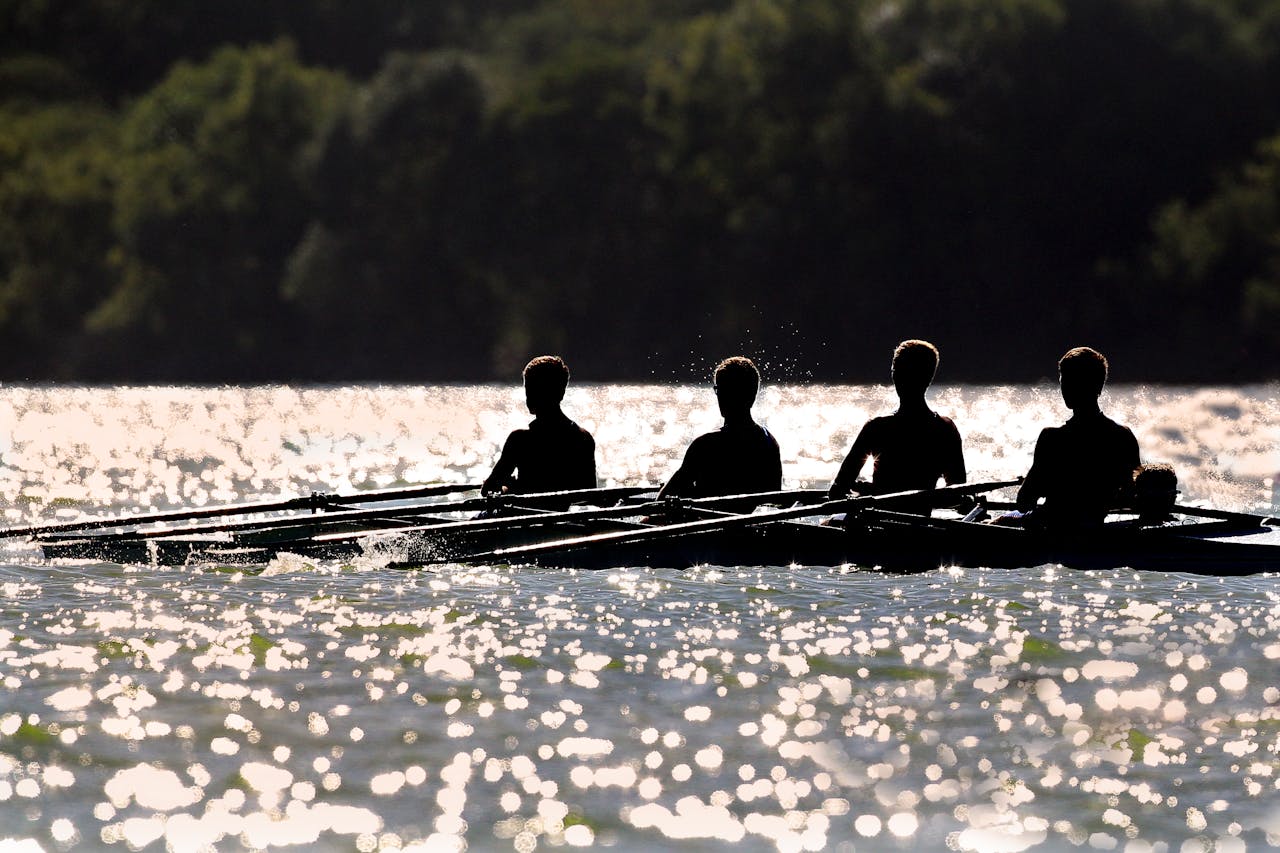 Silhouettes of rowers on a boat on a lake with trees in the background Photo: Patrick Case