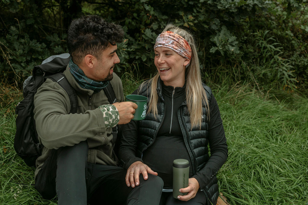 Couple sitting enjoying a drink after hiking wearing Ruffnek scarves, wrist band and head band, Green Tartan, Green Country Dogs and Scafell Pike Map